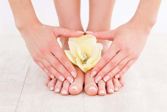 Beautiful manicure and pedicure. Close-up of young woman touching her feet while standing on hardwood floor